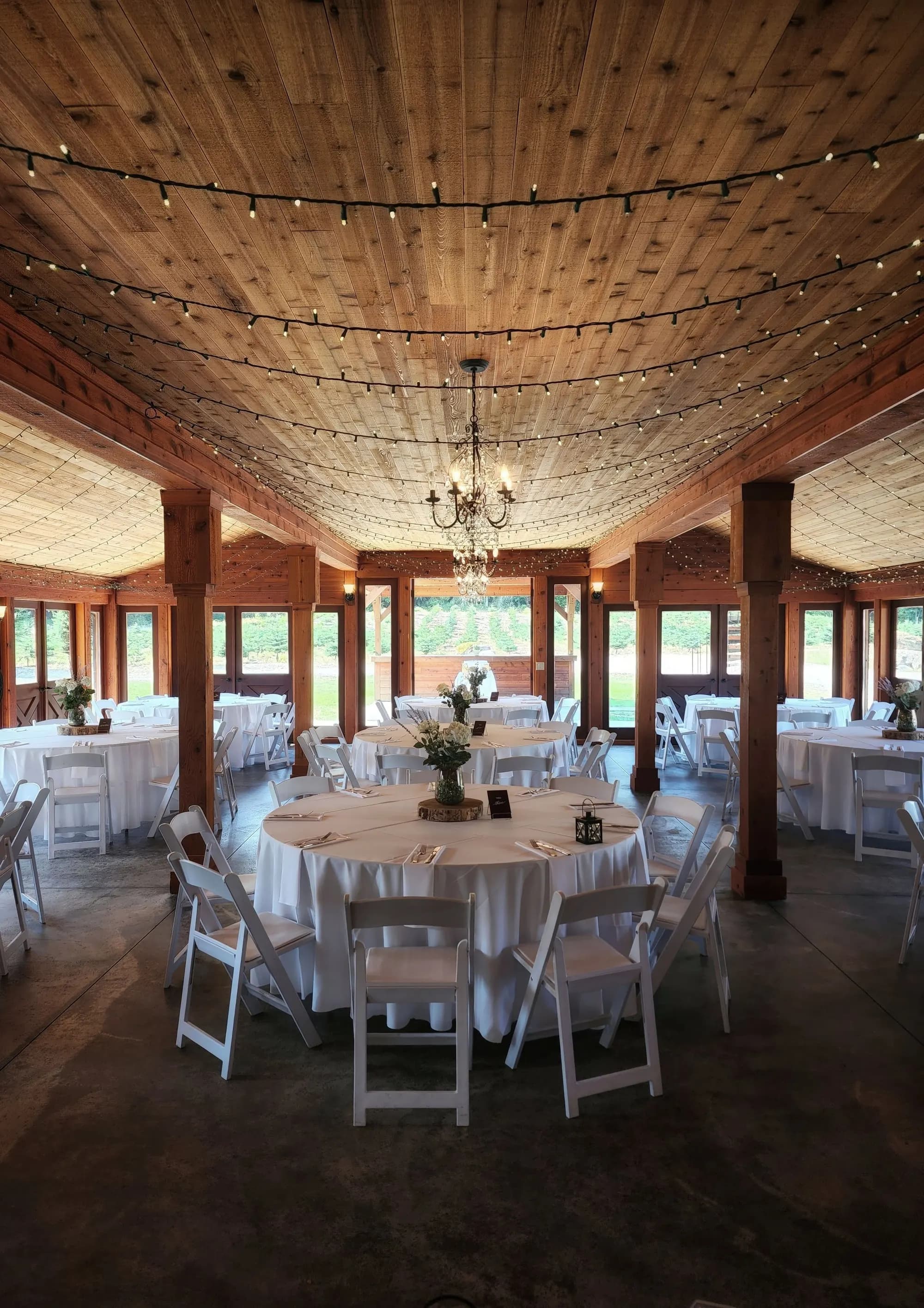 Rustic reception hall with a wooden beamed ceiling, string lights, and round tables